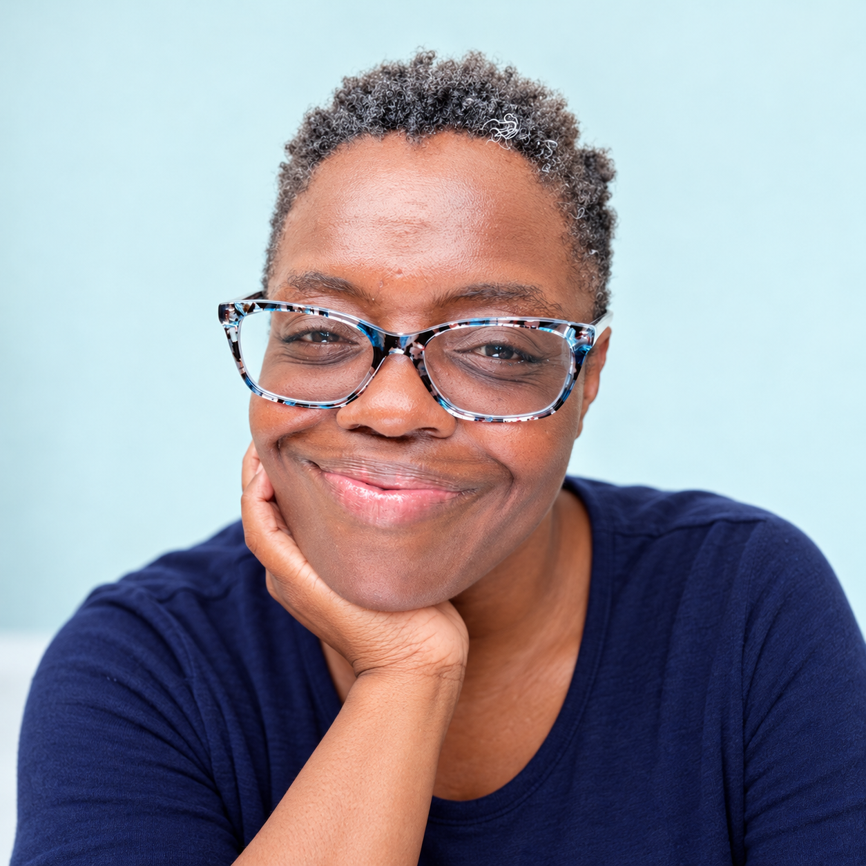 Portrait of Rafat Fields smiling, wearing patterned glasses and a navy top.